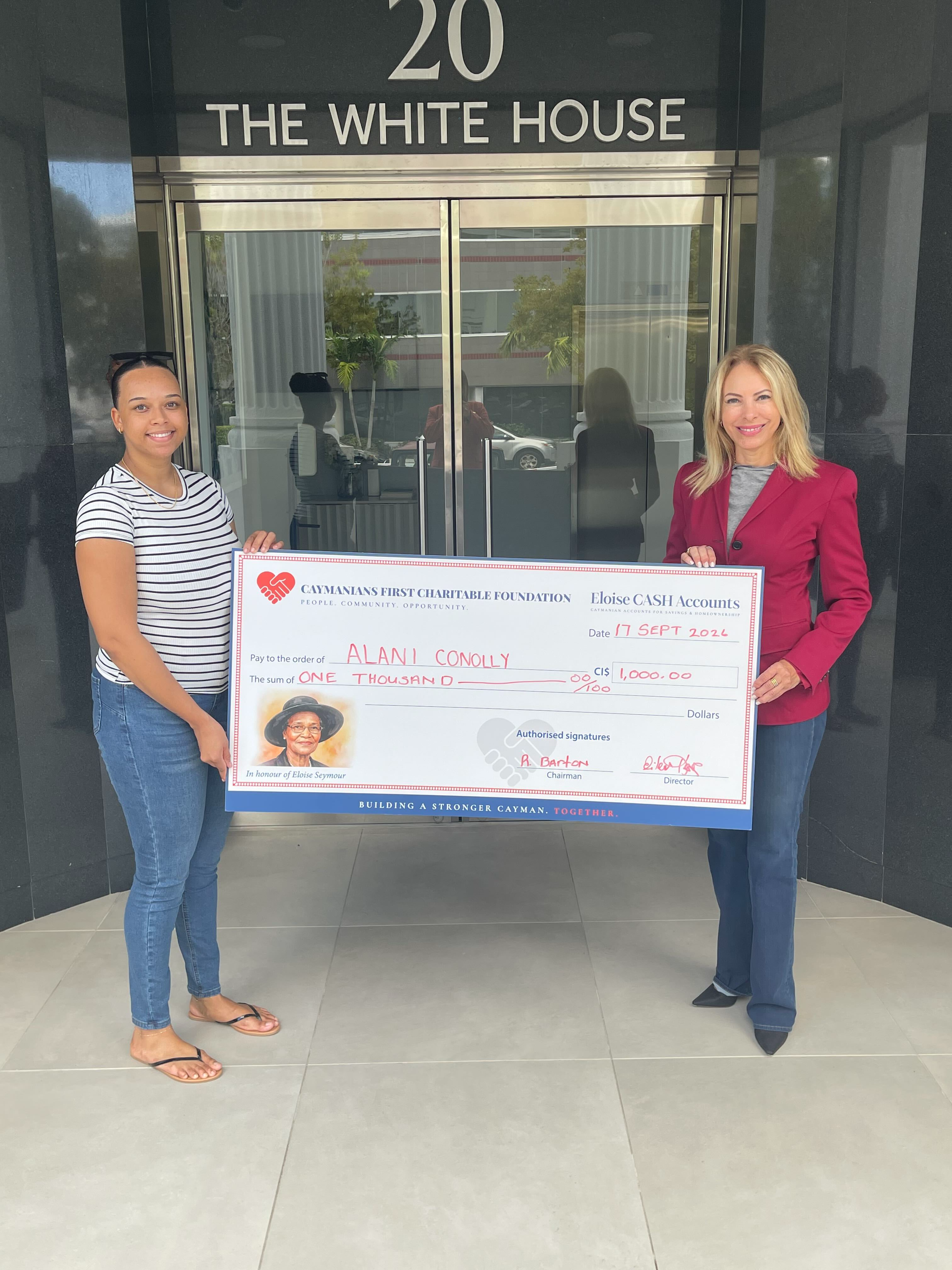 Two women holding an Eloise CASH Accounts presentation cheque for CI$1,000 made out to Alani Conolly.